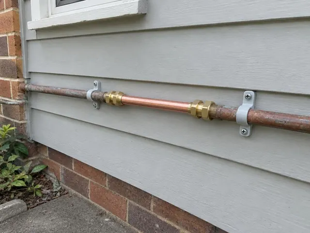 New copper pipe section on exterior weatherboard wall above brick base in Turramurra