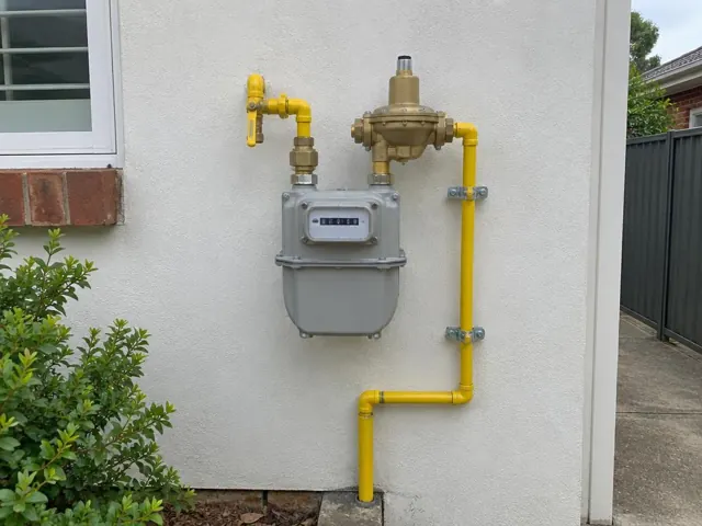 Exterior gas meter with new yellow pipework on a stucco wall beside a window in Thornleigh