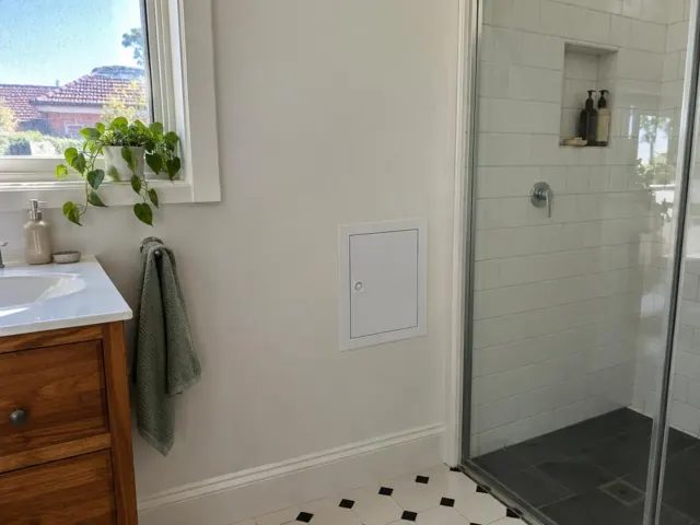 Bathroom wall with a small access panel beside a tiled shower and vanity in Hornsby